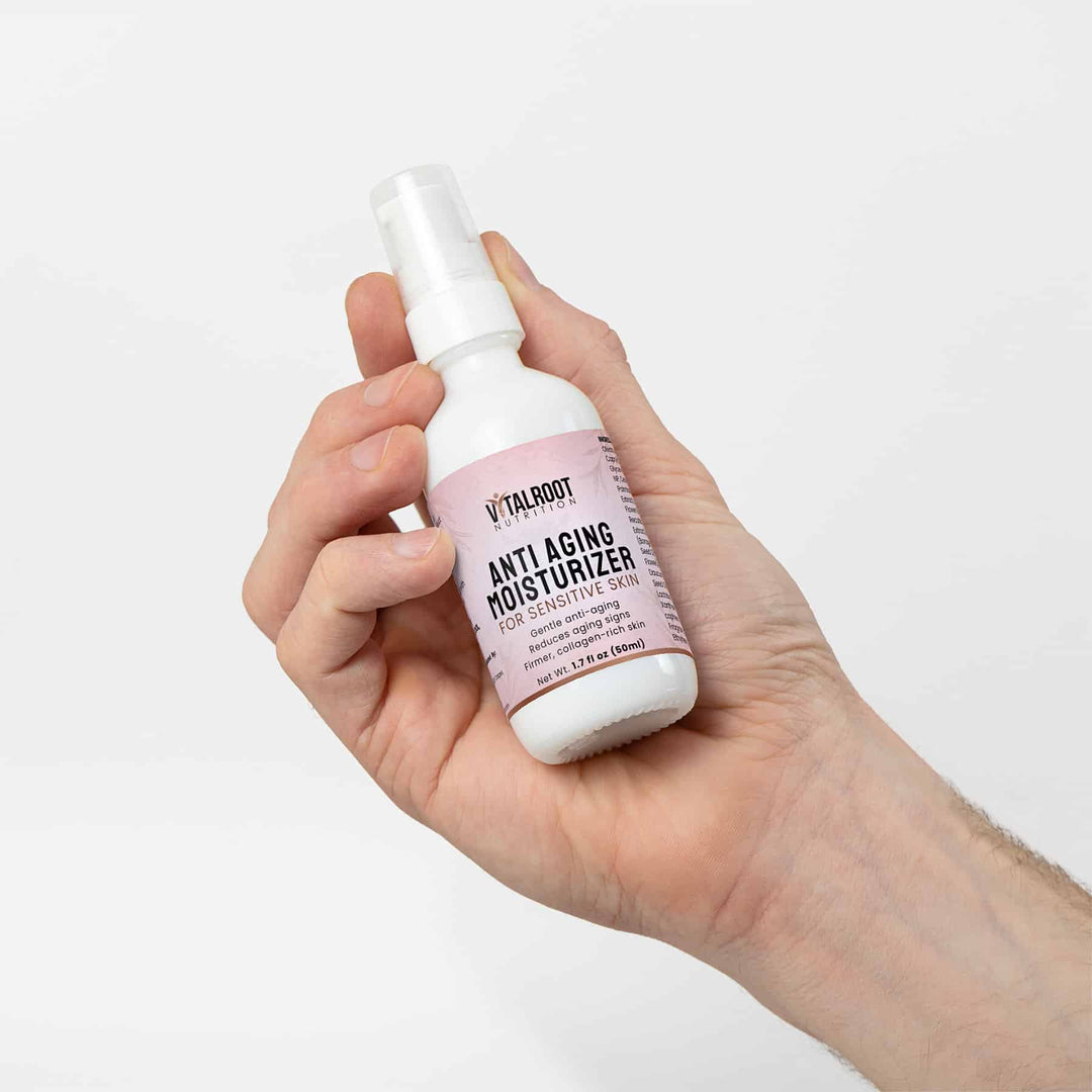 Hand holding a bottle of 'Vitalroot' anti-aging moisturizer against a white background