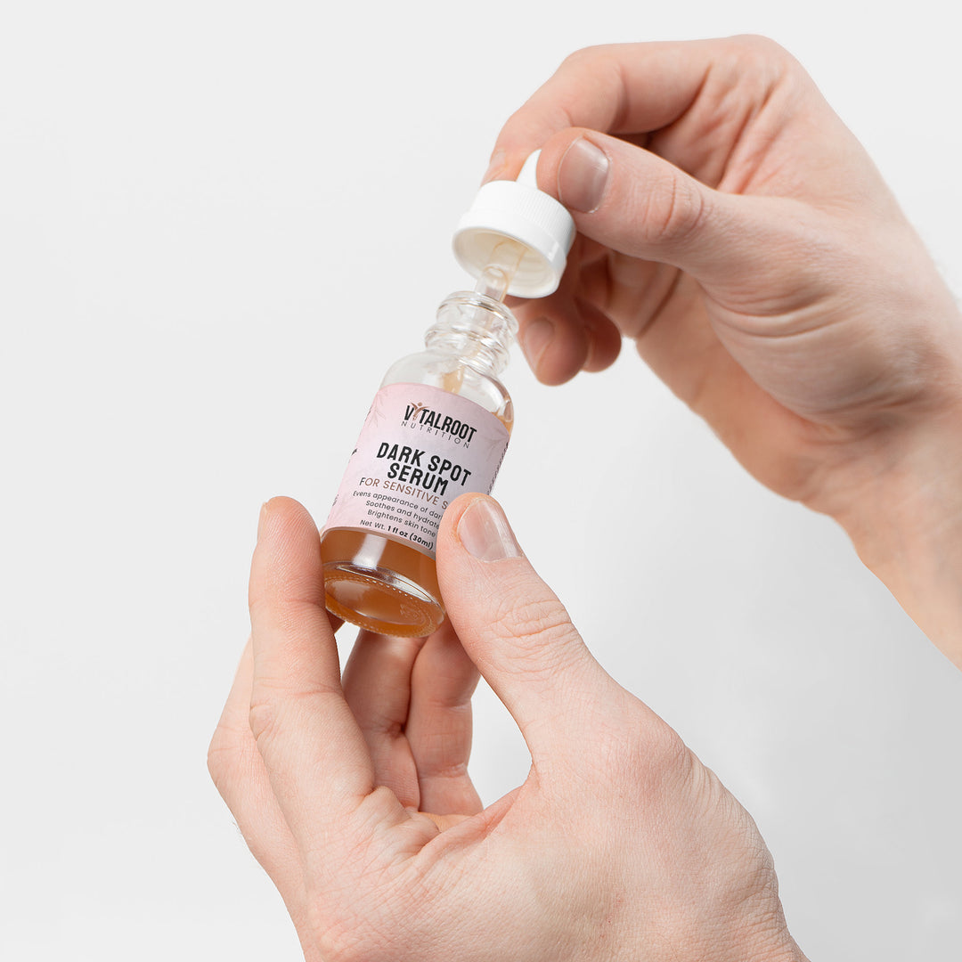 Hand holding a bottle of 'Vitality Dark Spot Serum' with a white background