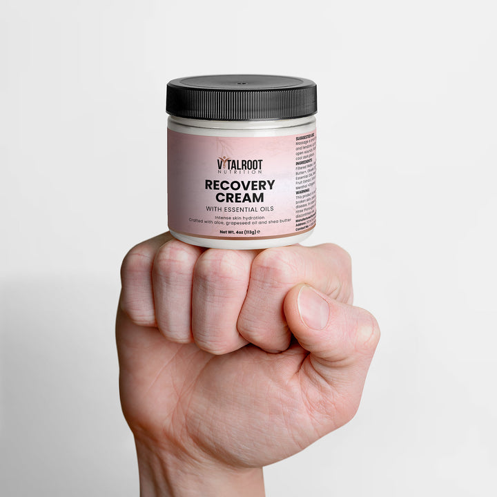 Hand holding a jar of Vital Root Recovery Cream against a light gray background