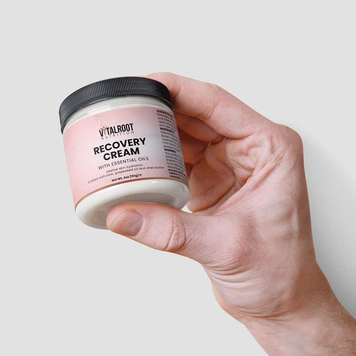 Hand holding a jar of Vitalroot Recovery Cream against a light background