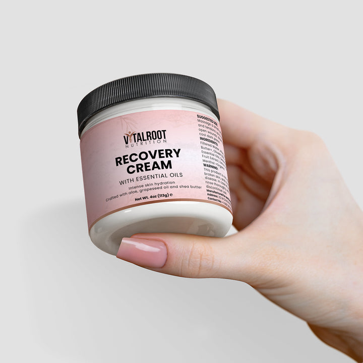 Hand holding a jar of Vitalroot Recovery Cream against a light background