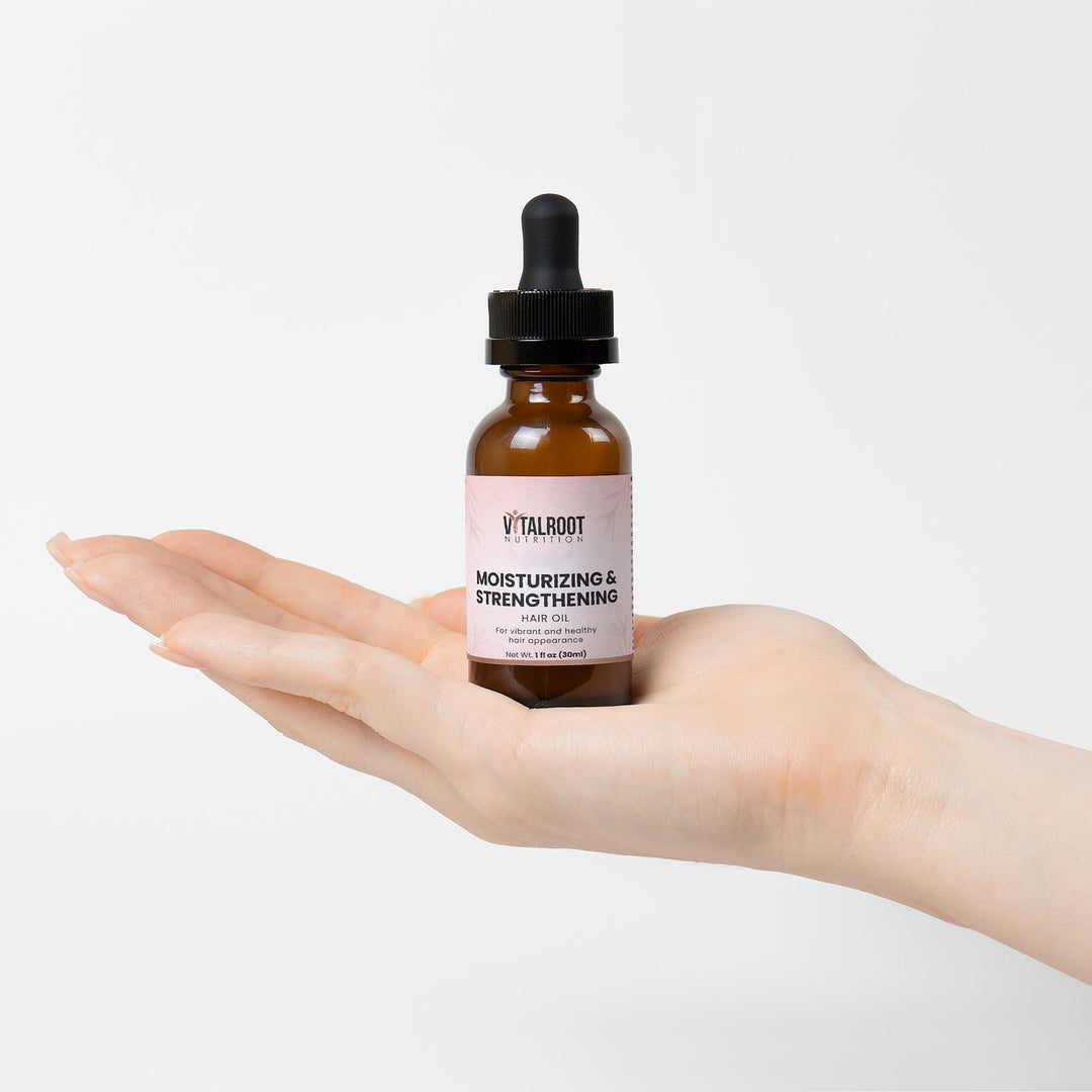 Hand holding a bottle of Vitalroot hair oil against a white background