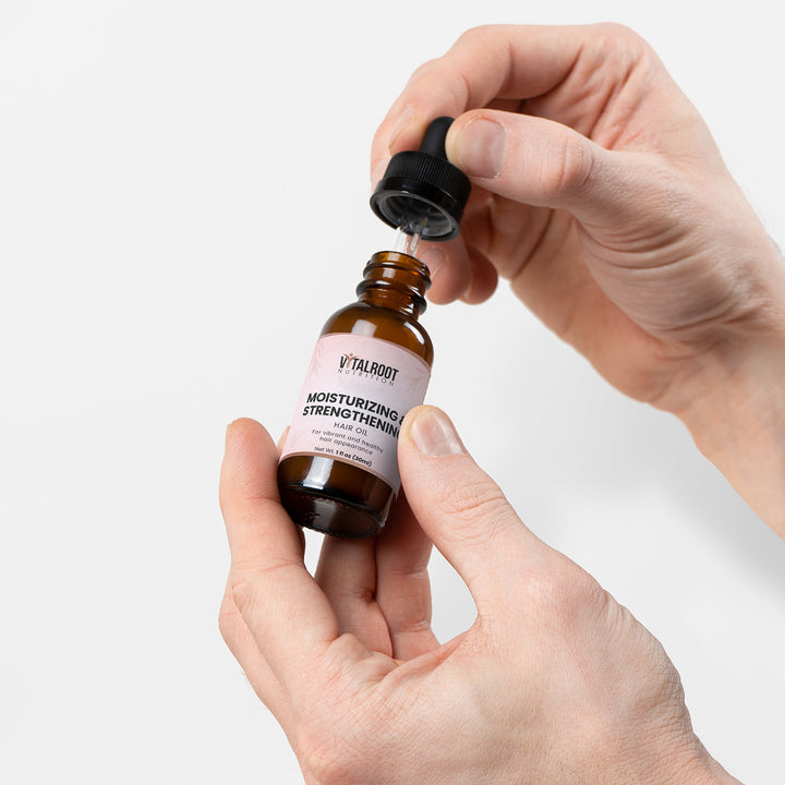 Hand holding a bottle of Vitalroot serum with a dropper against a white background