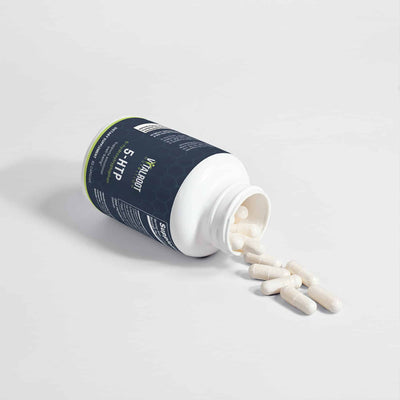 5-HTP bottle with capsules spilling out beside the bottle on a white surface.
