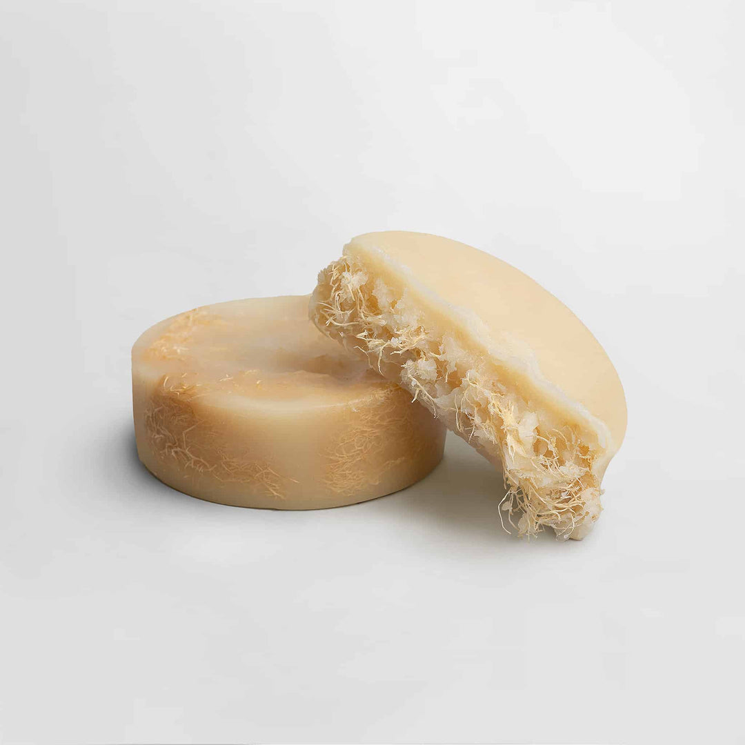 Two pieces of natural soap with a fibrous texture on a light gray background