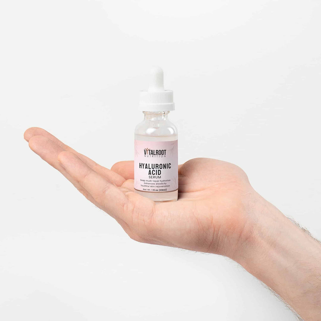 Hand holding a bottle of Vitalroot Hyaluronic Acid on a white background