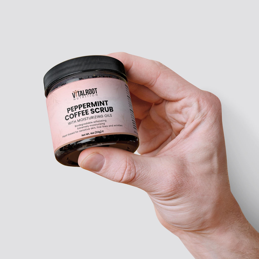 Hand holding a jar of peppermint coffee scrub with a plain background