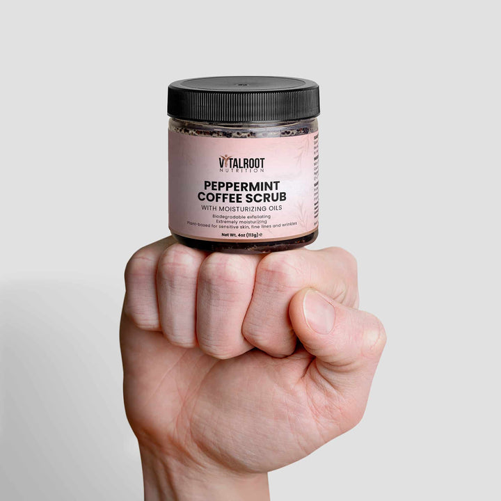 Jar of peppermint coffee scrub held in a hand against a light gray background