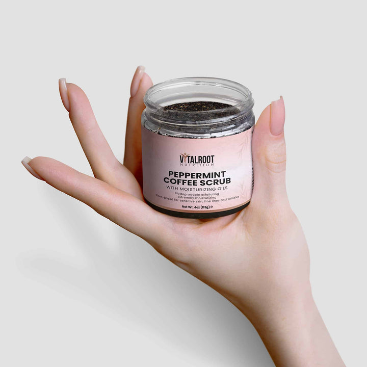 Hand holding a jar of peppermint coffee scrub with a plain background