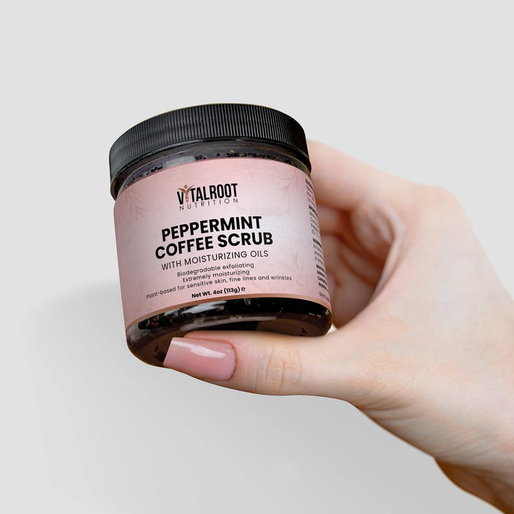 Hand holding a jar of Vital Root Nutrition peppermint coffee scrub against a light gray background
