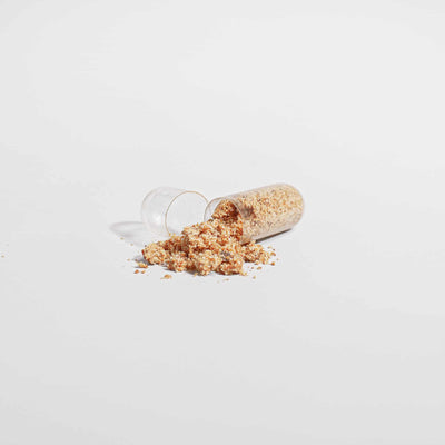 Bee Pearl capsule opened with powder spilling out onto a white background.