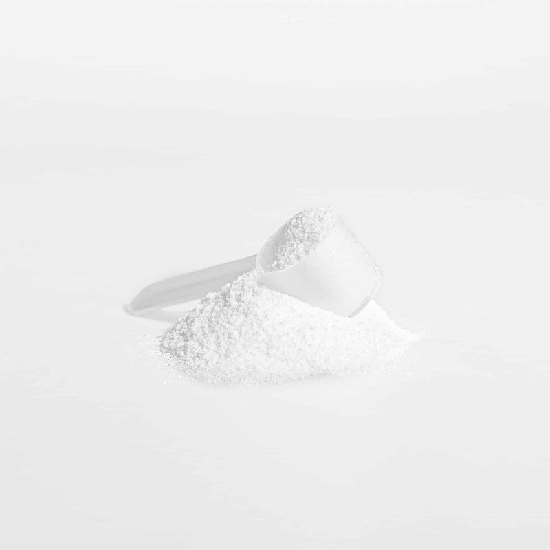 Scoop of Creatine Monohydrate powder with a pile of powder beside it on a white background.